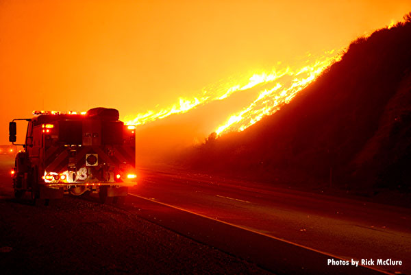 在加利福尼亚州文图拉县，一辆消防车停在高速公路上，背景是一场野火肆虐。