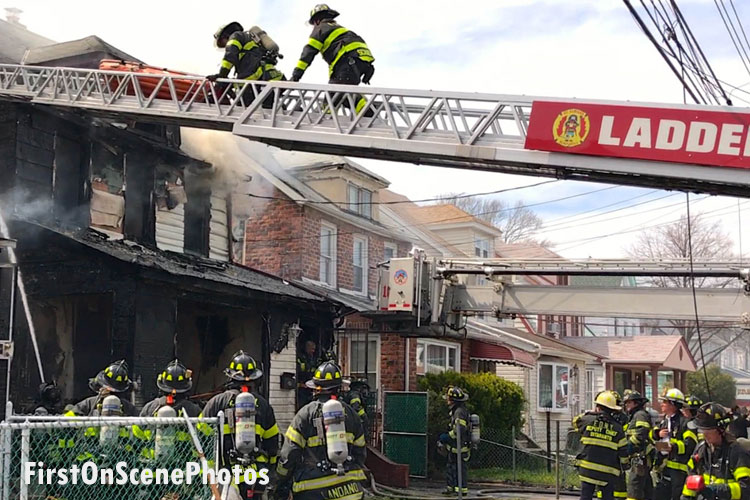 消防队员在梯子上和在一处致命的房屋火灾现场外的街道上
