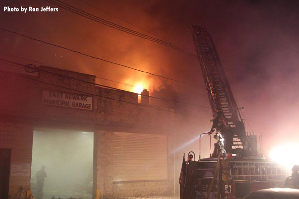 大火从东纽瓦克(NJ)建筑的屋顶上射出，在前景中，一架空中飞机正在运行。