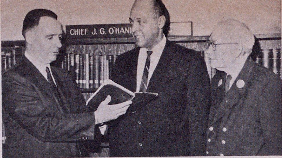 退休的副局长James G. O 'Hanlon(左)把他送给纽约消防局图书馆的一卷珍贵藏书拿给局长Robert 0。Lowery和部门图书管理员，荣誉副局长Clarence Meek，在O 'Hanlon私人图书馆的正式验收和部门图书馆扩建设施的奉献仪式上。