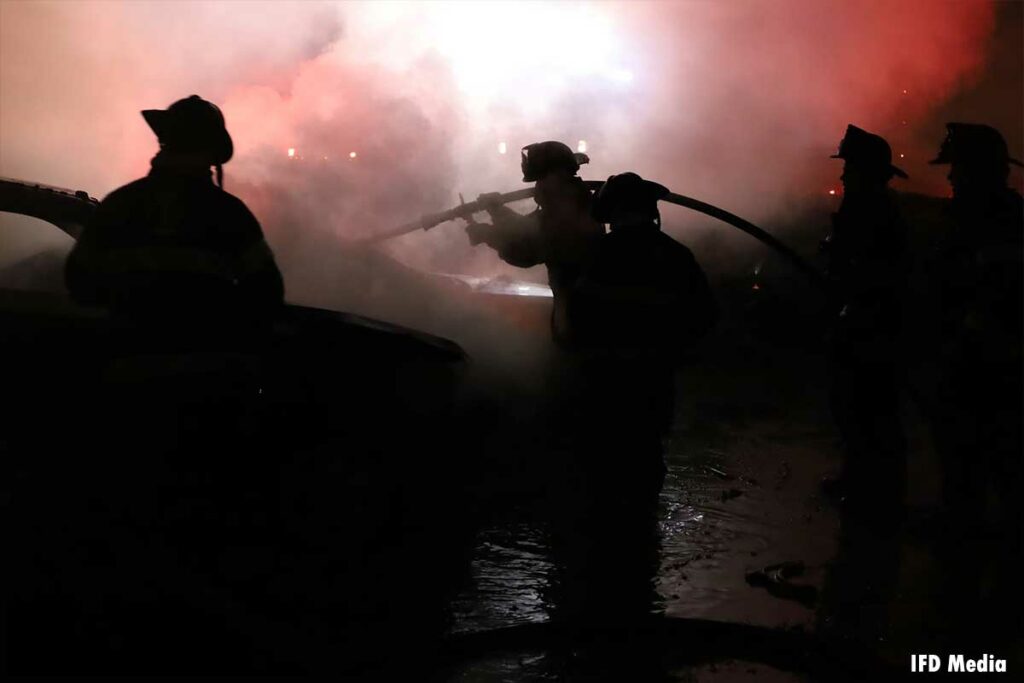 消防队员肩上扛着水绳，向着火的车辆喷水